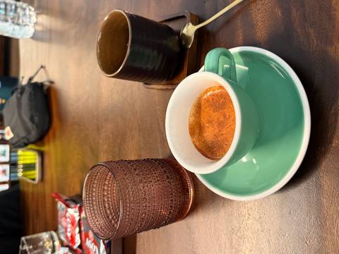 Espresso in a turquoise cup on wooden table beside textured glass and other café items in Hanoi.