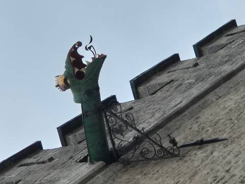 Decorative green dragon waterspout with crown juts from stone wall.