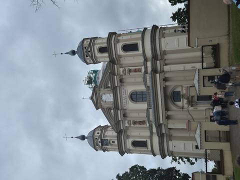Visitors enter baroque church with twin towers under grey skies.