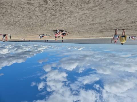 Relaxed beachgoers on wide sandy shore beneath scattered clouds.