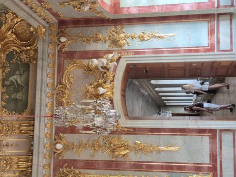 Lavish baroque interior with gold stucco, chandelier and visitors exploring.