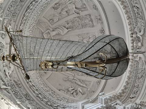 Intricate ship-shaped crystal chandelier hanging from ornate church ceiling.