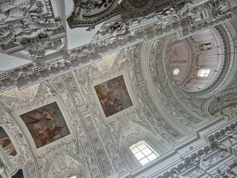Highly ornate stucco ceiling and mural panels inside baroque church.