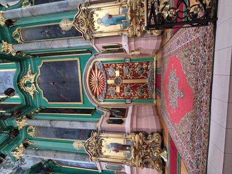 Colourful Orthodox iconostasis with ornate cross and carpets.