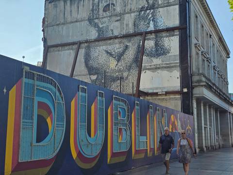 Street construction hoarding with large DUBLIN lettering and mural art, two pedestrians walking