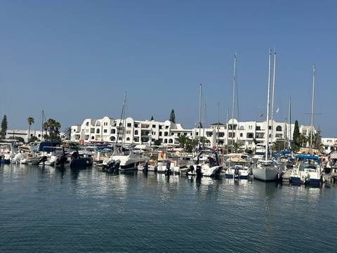 Marina filled with sailboats and motor yachts in front of white Moorish-style resort buildings under a clear sky.