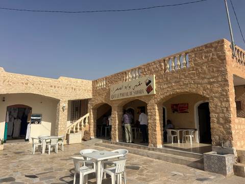 Stone-built roadside cafe with shaded terrace and Arabic signage offering refreshments in the Tunisian desert heat.