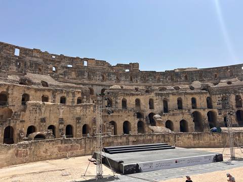Interior stone arches and tiered seating of the ancient Roman amphitheatre at El Jem lit by midday sun.
