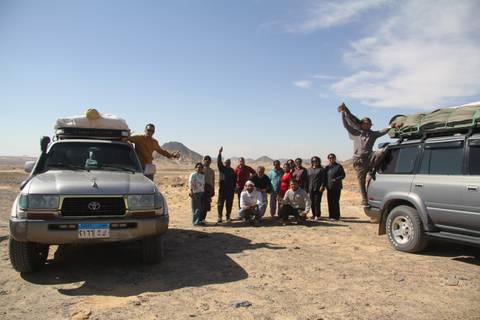 Adventure group posing between two loaded 4x4 vehicles in the barren Egyptian desert.