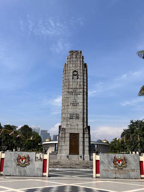Stone war memorial obelisk standing in a green park under clear sky