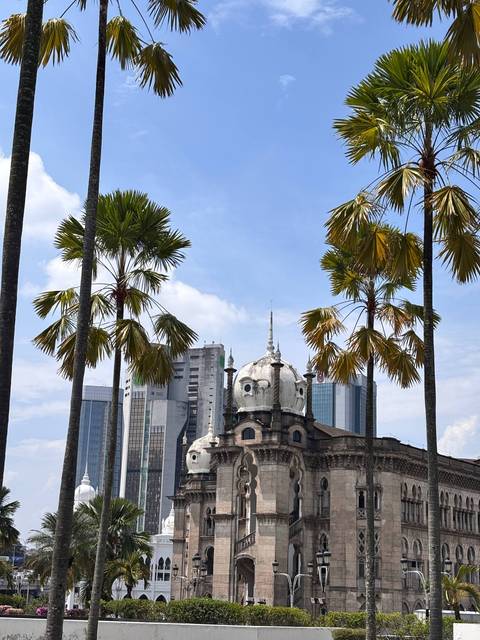 Colonial dome building framed by tall palm trees against bright blue sky in Kuala Lumpur