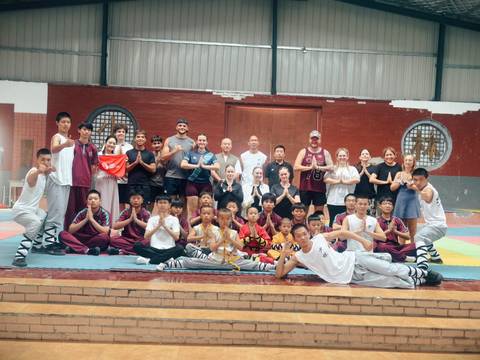 Large international group of students and Shaolin monks pose together inside a martial arts training hall.