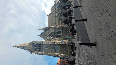 Stone Gothic Christ Church Cathedral rises above pedestrians on a bright day in Dublin.