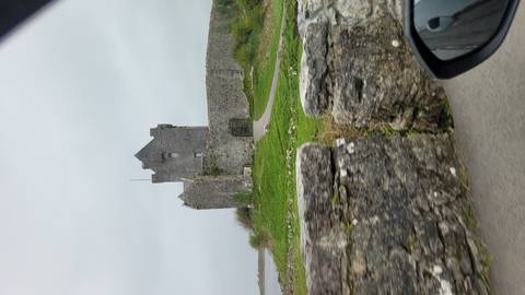 Stone tower house and curtain wall seen from a passing car on a cloudy day.