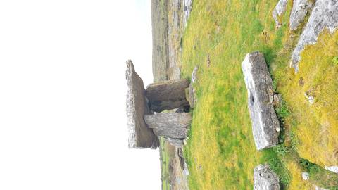 Ancient stone dolmen standing on a grassy limestone plain under a bright white sky.