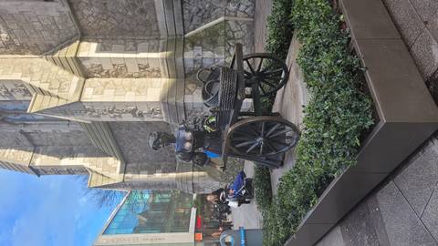Bronze statue of Molly Malone with wicker cart set in a pedestrian street beside a stone church, several shoppers nearby.