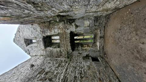 Rugged interior walls and window openings of a stone medieval ruin viewed from ground level.