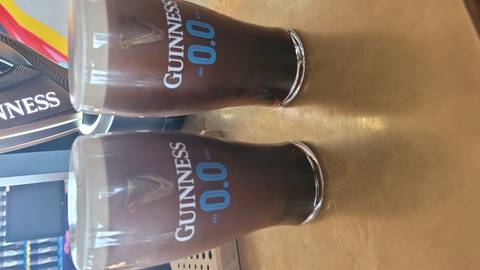 Two pints of Guinness 0.0 beer on a bar counter with brewery taps in the background.
