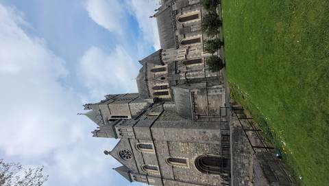 Impressive grey-stone Christ Church Cathedral towering above a green lawn under broken clouds.