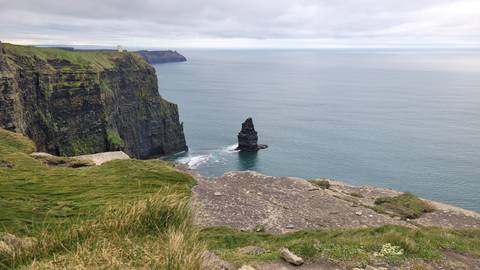 Sheer green cliffs dropping into the Atlantic with a sea stack and distant lookout tower.