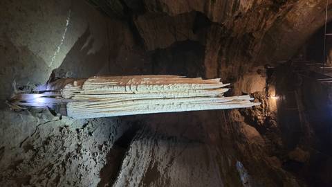 Massive illuminated stalactite hanging in a dimly lit limestone cave chamber.