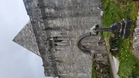 Weathered stone abbey wall with gothic doorway and ancient headstone in foreground.
