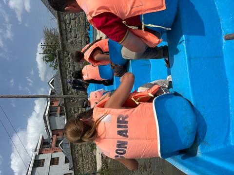 Tourists wearing life jackets seated in blue boat preparing for lake excursion.