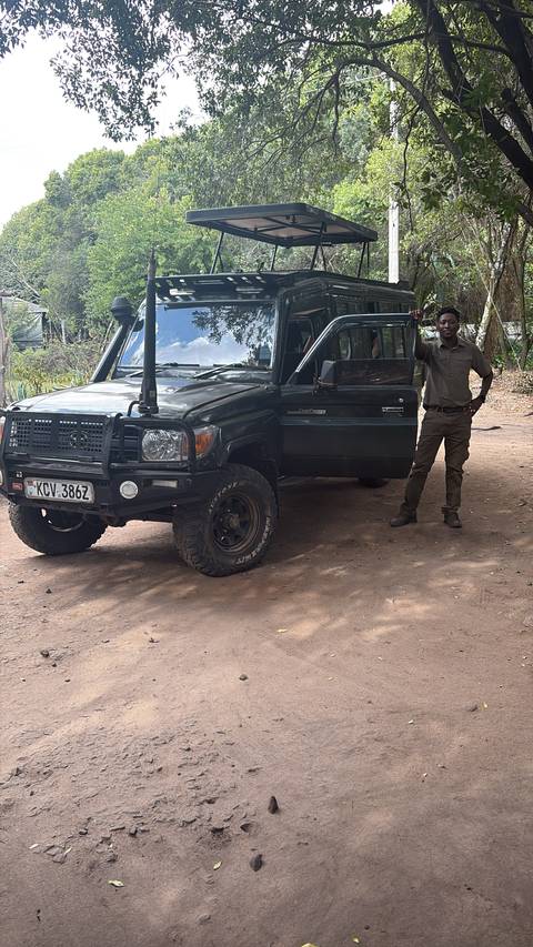 Safari guide standing beside rugged Land Cruiser in shaded camp area.