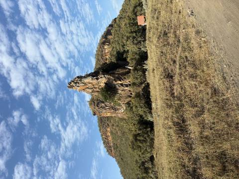 Jagged rock outcrop rising above grassy plain beneath patterned blue-and-white sky.