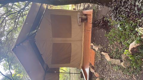 Canvas safari tent with wooden deck set amid a shaded camp area.