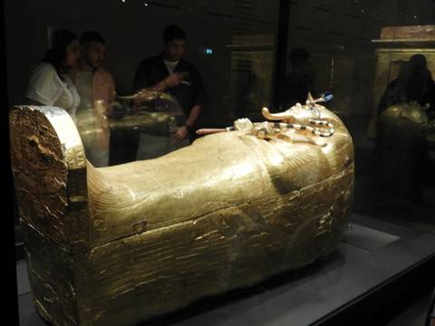 Golden sarcophagus of Tutankhamun displayed in museum glass case with visitors observing