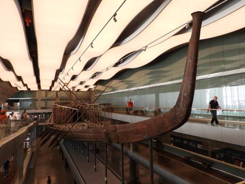 Ancient solar boat displayed inside modern gallery with undulating ceiling panels