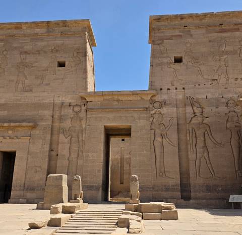 Stone facade of Philae Temple with faint reliefs under clear blue sky