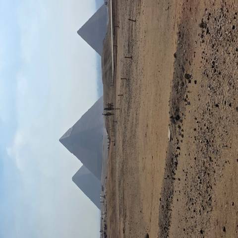 Distant pyramids rising above sandy plateau with hazy morning sky