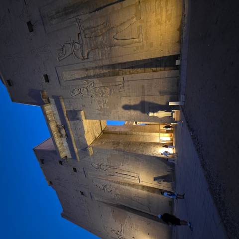 Illuminated entrance of Egyptian temple at blue hour with tall shadow on wall