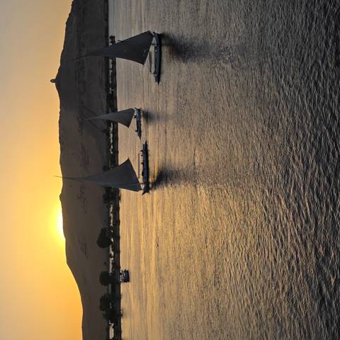 Two feluccas sailing on the Nile at sunset with golden reflections on the water