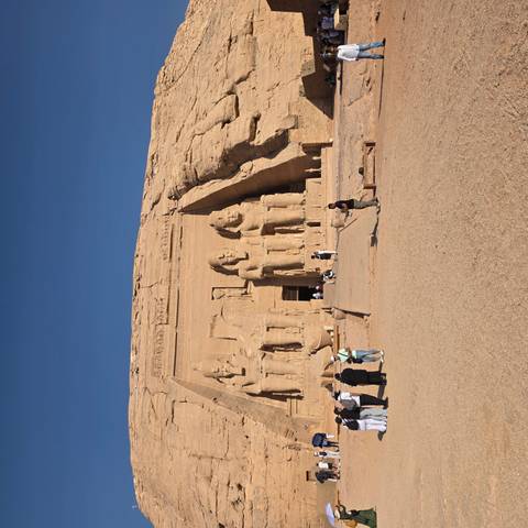 Rock-hewn façade of Abu Simbel with colossal seated statues and visitors in foreground