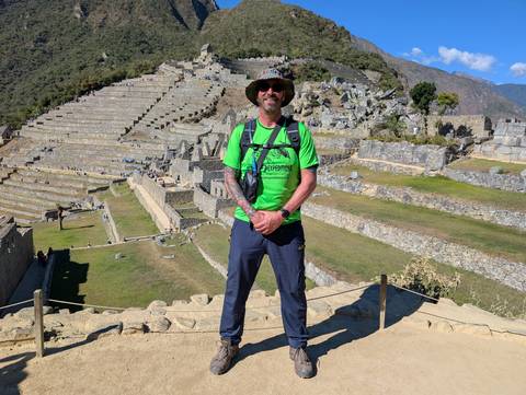 Hiker in neon green shirt stands proudly on Machu Picchu terraces with stone ruins cascading behind.