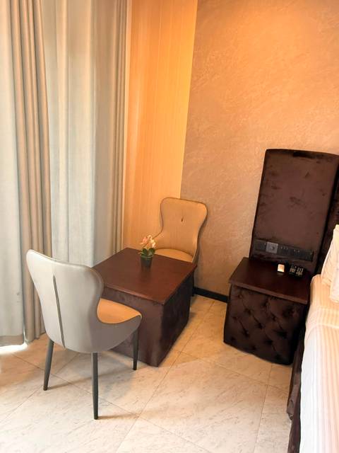 A small wooden table with two upholstered chairs in the corner of a hotel room beside tall curtains.