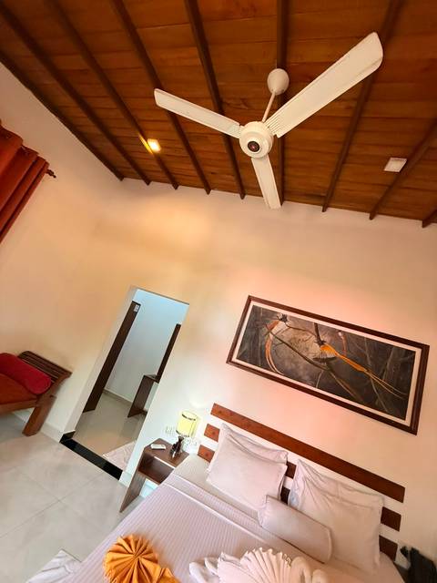 Angled view of a hotel room ceiling with exposed beams, red curtains and a framed bird painting.