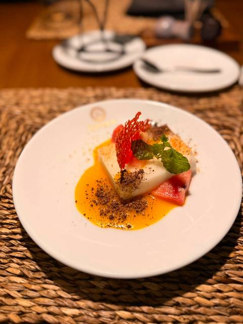 A gourmet plated dessert with bright fruit, mint and sauce artfully arranged on a white plate.