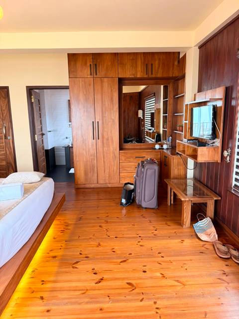 Wood-paneled hotel room interior with wardrobe, luggage, wall-mounted TV and a glimpse of the bathroom.