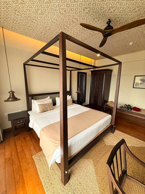 Another angle of a four-poster bed with beige linens, bedside table and wardrobe in a polished room.