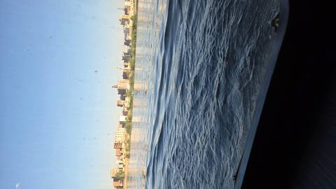 View across a wide river toward a modern city skyline under a clear blue sky, seen from a low vantage near the water.