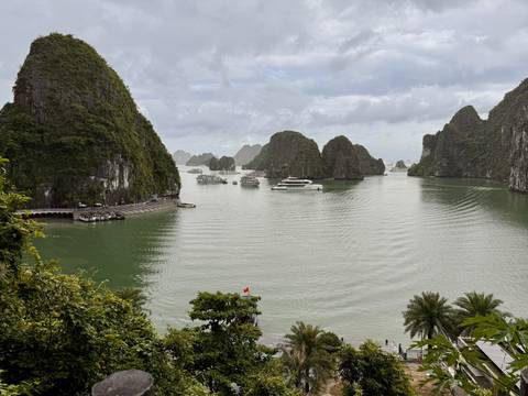 Limestone karst islands rise from emerald waters of a broad bay dotted with cruise boats.