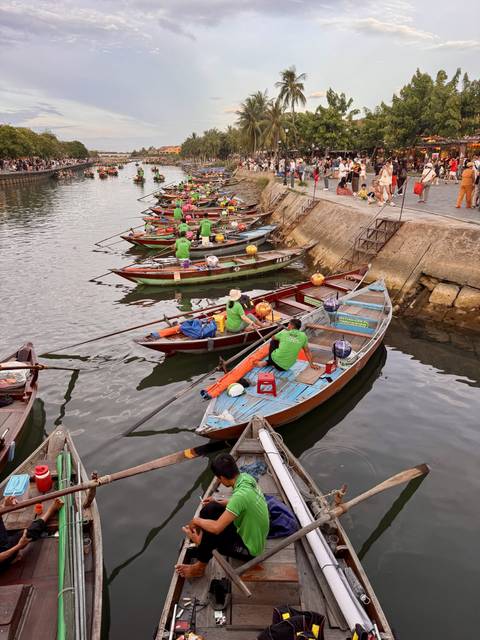 Rowers in bright green shirts prepare colorful wooden boats alongside a stone quay.