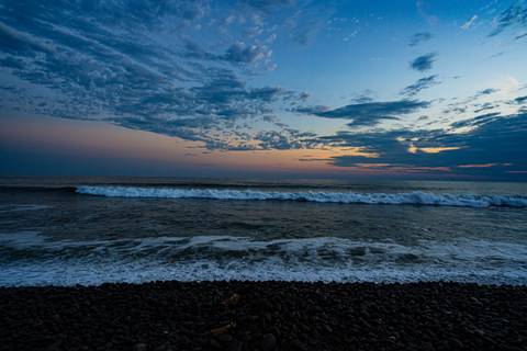 Twilight view of ocean waves rolling toward a rocky shoreline under a dramatic, colorful sky