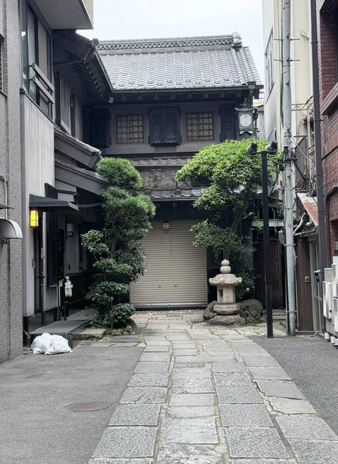 Quiet traditional Japanese alley with closed wooden shutters, manicured trees and a stone lantern.
