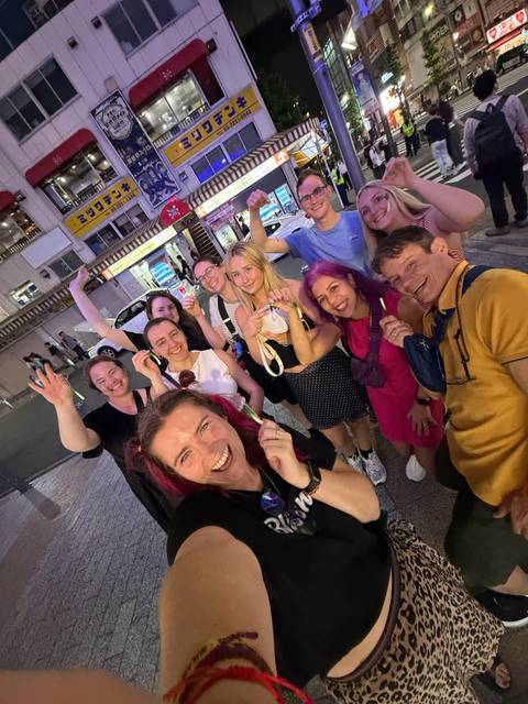 Nighttime street selfie of a cheerful travel group under neon signs in a busy Tokyo district