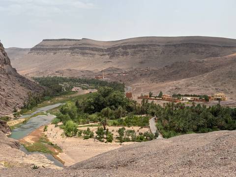 Wide desert valley with a winding river, palm groves and small villages beneath layered cliffs.